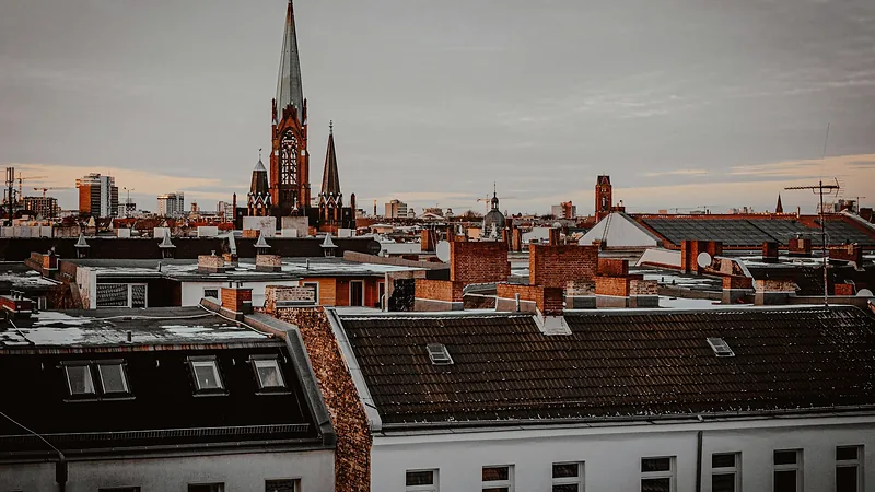 Blick über Berliner Altbaudächer mit Gauben und Schornsteinen, im Hintergrund ein Kirchturm